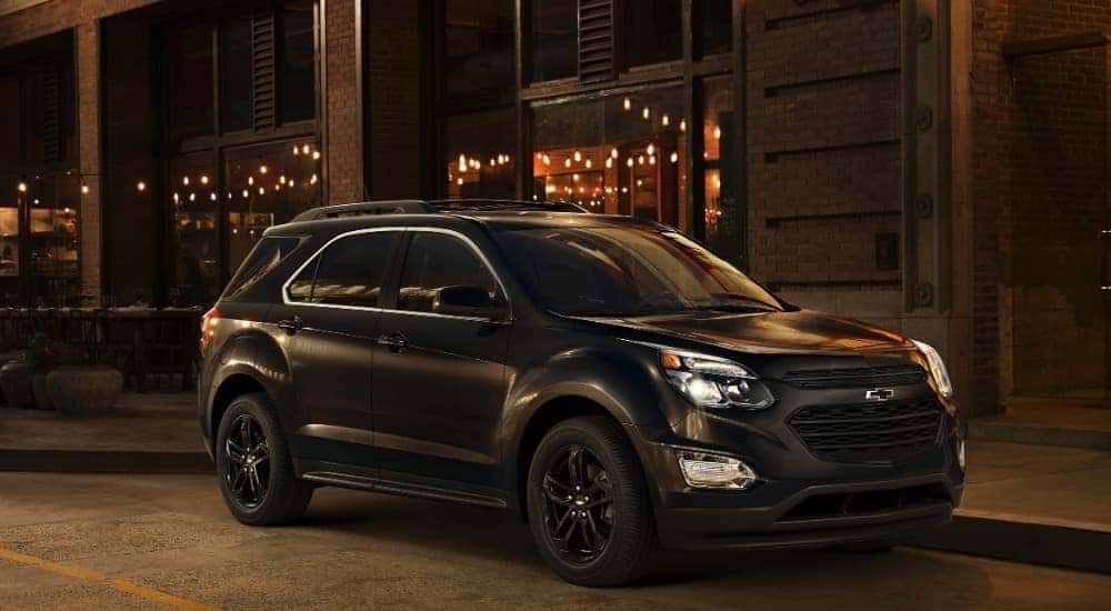 Black 2017 Chevrolet Equinox SUV parked in front of a brick building with strings of lights in the windows