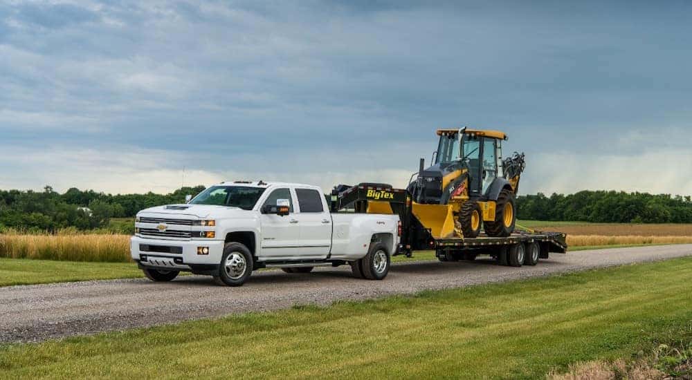 White 2017 Chevrolet Silverado 3500HD pulling construction equipment down a paved road