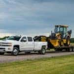 Black 2017 Chevrolet Silverado 3500HD pulling a construction vehicle down a dirt road next to large green fields