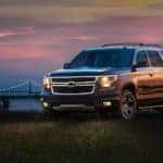 Black 2017 Chevrolet Tahoe parked in grass in front of a city skyline with its lights on