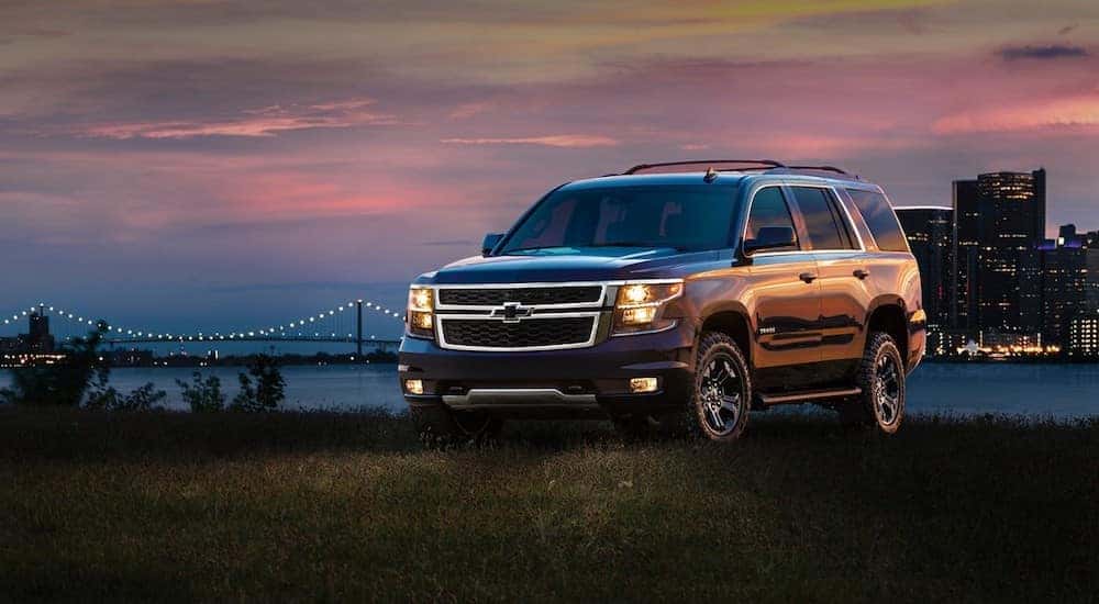 Black 2017 Chevrolet Tahoe parked in grass in front of a city skyline with its lights on