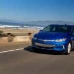 Blue 2017 Chevrolet Volt sedan driving down a paved road past an ocean shore