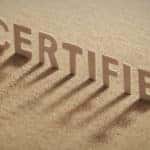 Brown cardboard letters that spell out "CERTIFIED" standing up on a brown surface