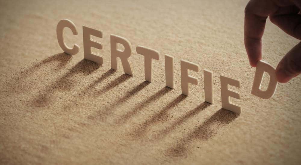 Brown cardboard letters that spell out "CERTIFIED" standing up on a brown surface