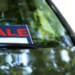 Black, white, and red "SALE" sign in the front window of a black vehicle