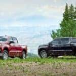 A red and a blue 2020 Chevy Silverado are parked in front of pine trees.