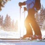 A man is shown cross country skiing with the sun rising over pine trees in the backround.