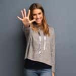 Woman in a tan sweater smiling and holding five fingers up and reaching toward the camera