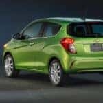 Back to front view of a lime green 2016 Chevrolet Spark parked in an all-black room