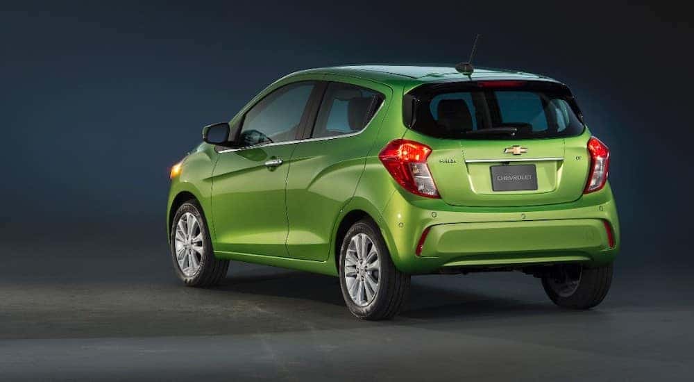 Back to front view of a lime green 2016 Chevrolet Spark parked in an all-black room
