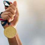 Hand holding a gold award medal by the red, white, and blue ribbon tied on it