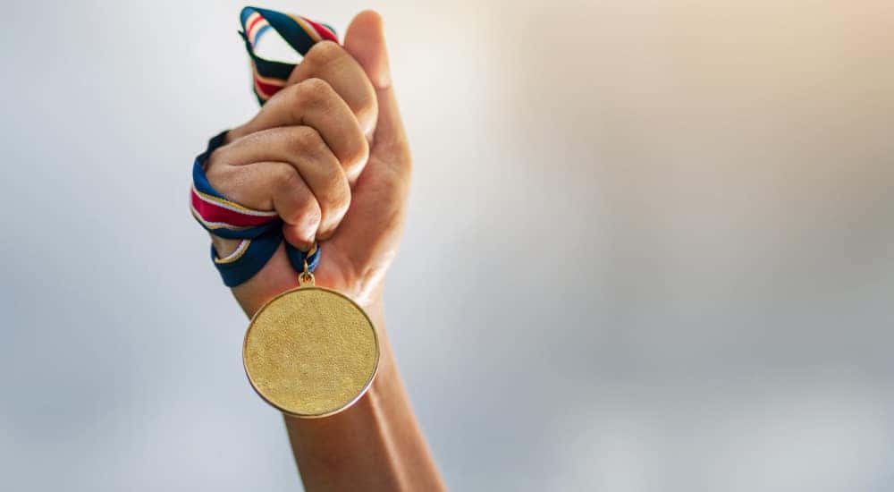 Hand holding a gold award medal by the red, white, and blue ribbon tied on it
