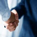 Man in a suit shaking hands with someone wearing a light blue button-up shirt