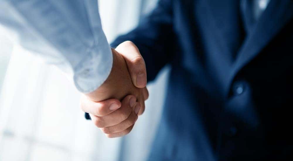 Man in a suit shaking hands with someone wearing a light blue button-up shirt