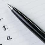 Black pen on top of a notebook with black binding and white lined paper that has black numbers one through four along the side