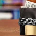 Black leather wallet with cash sticking out wrapped in chains with a padlock on it