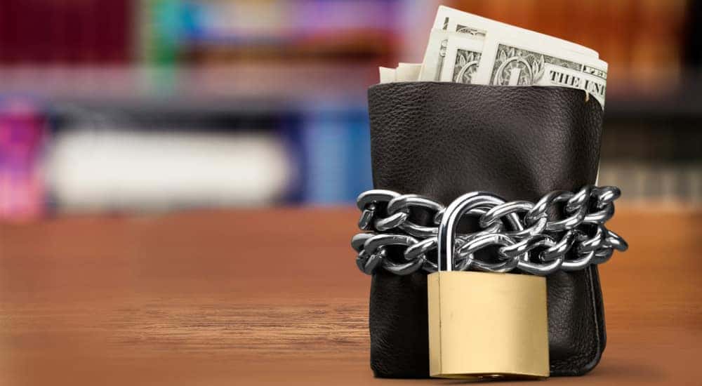 Black leather wallet with cash sticking out wrapped in chains with a padlock on it