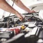 Man in a blue apron working underneath the open hood of a vehicle