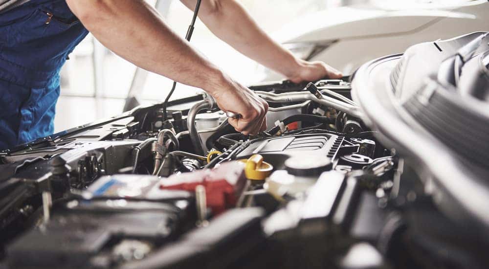 Man in a blue apron working underneath the open hood of a vehicle