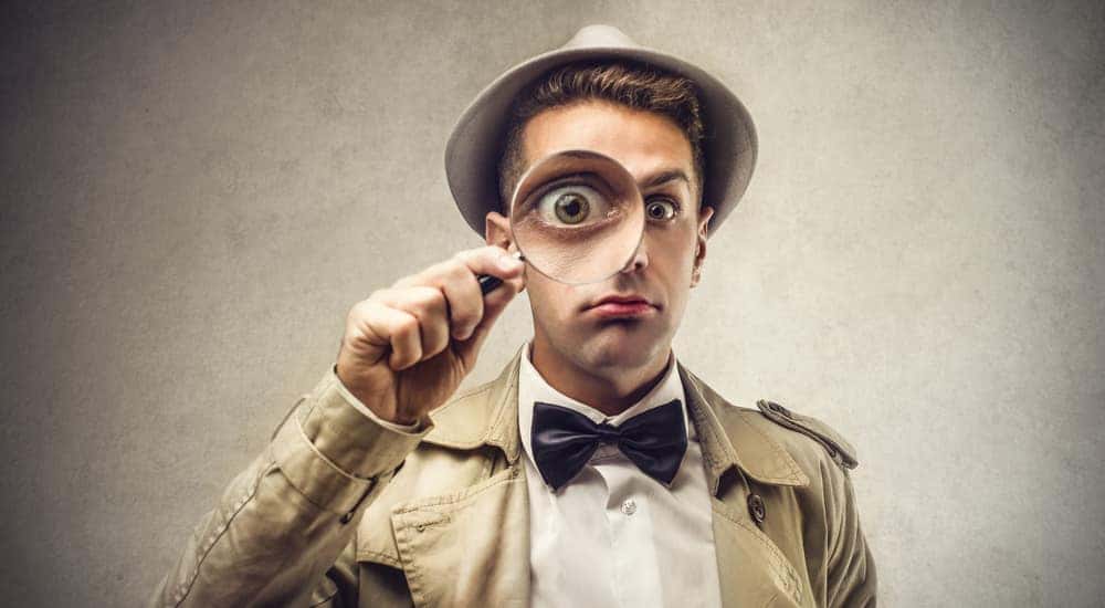 Man in a bow tie with a magnifying glass to his face enlarging his eye