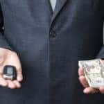 Man in a suit holding out a car key in one hand and cash in the other