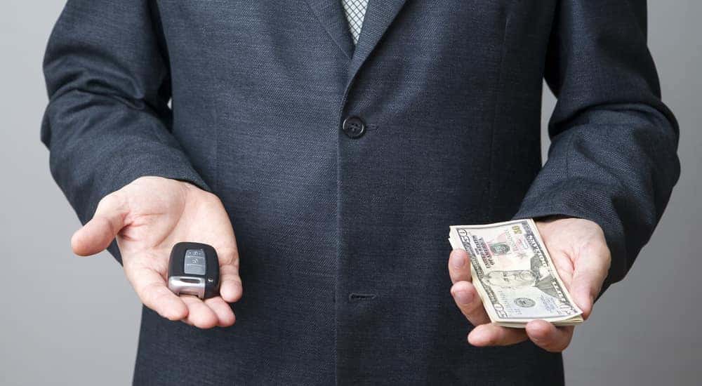 Man in a suit holding out a car key in one hand and cash in the other