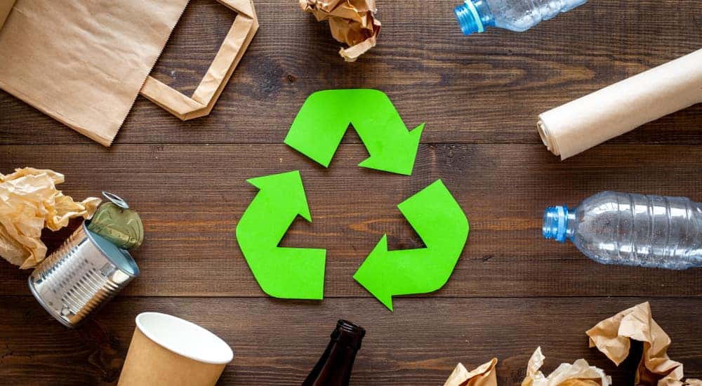 Green recycling symbol sitting on a wooden table in the middle of various paper and plastic products