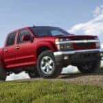 Red 2012 Chevrolet Colorado driving over a grassy hill through a dirt path