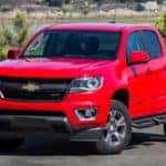 Red 2016 Chevrolet Colorado pickup truck parked in front of a body of water and a couple of trees
