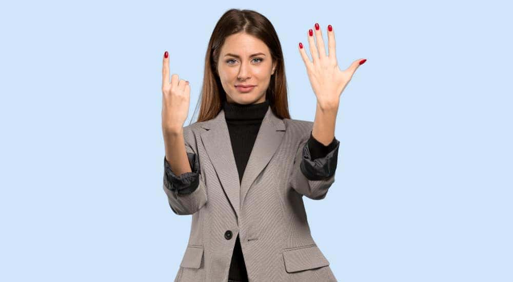 Businesswoman in a blazer holding up six fingers against a blue background