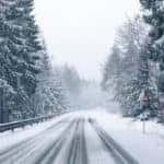 Snowy winter road next to a guardrail and tall, snow-covered trees