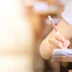 Person in a white shirt writing on paper on a wooden desk