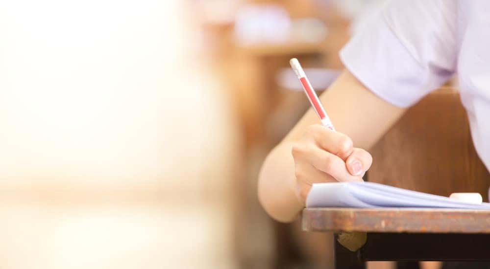 Arm of a woman in a white shirt leaning on a desk and writing