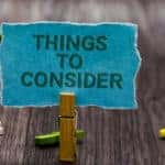 Various colored clothespins spread across a wooden table behind one standing up and holding a sign that says "THINGS TO CONSIDER"