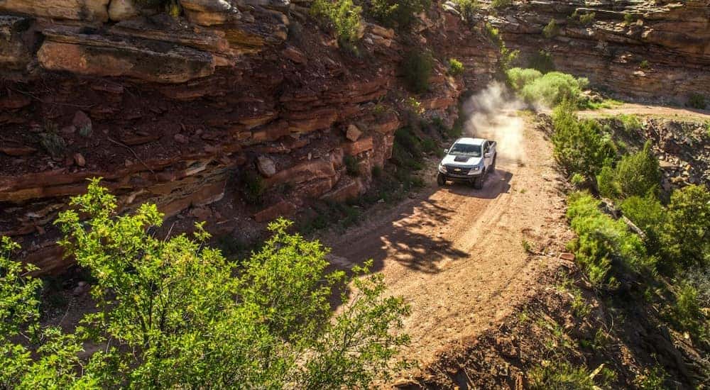 White 2017 Chevrolet Colorado pickup truck driving down a dirt path next to a cliff