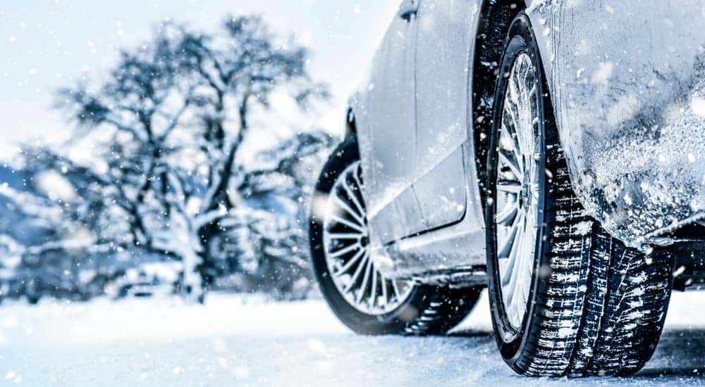 Tires on a silver vehicle driving down a snowy road past snow-covered trees