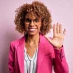 Woman in a pink blazer standing with five fingers up in front of a pink wall