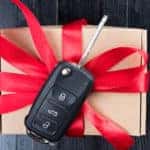 Car key on top of a small brown gift box tied with red ribbon on a black table
