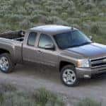 Grey 2009 Chevrolet Silverado driving down a dirt road past green grass