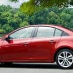 Red 2011 Chevrolet Cruze sedan parked on pavement in front water and trees