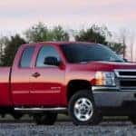 Red 2011 Chevrolet Silverado 2500HD truck parked on pavement in front of green trees
