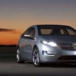 Grey 2011 Chevrolet Volt with its lights on parked in front of a dark sunset