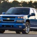 Blue 2012 Chevrolet Colorado pickup truck parked in front of a river, grass, and trees