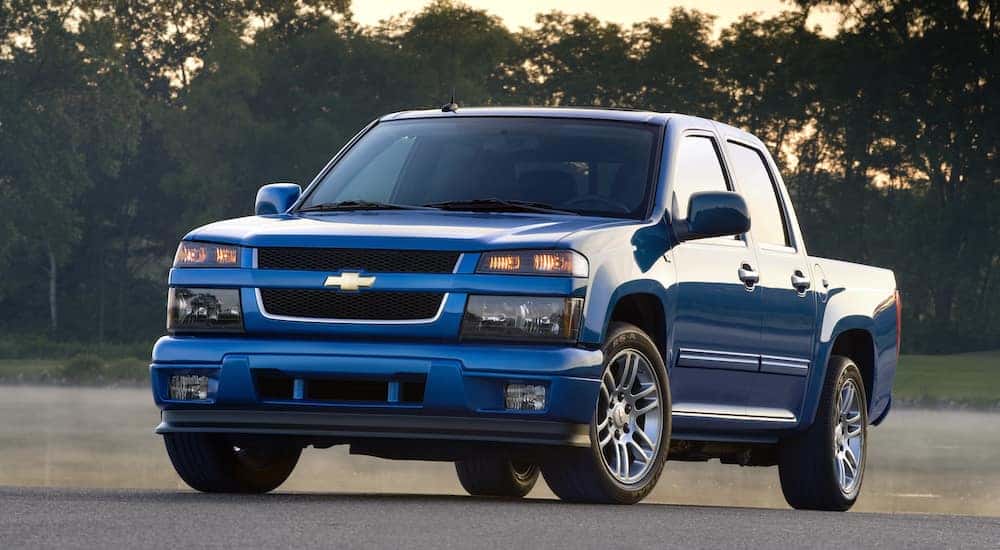 Blue 2012 Chevrolet Colorado pickup truck parked in front of a river, grass, and trees