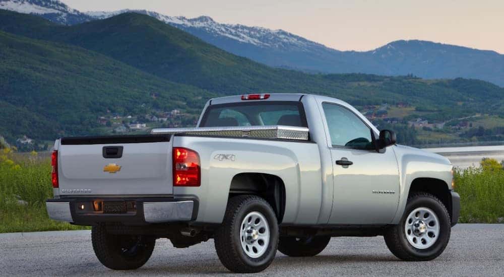 Silver 2013 Chevrolet Silverado 1500 pickup truck parked on pavement in front of tall mountains