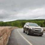 Tan 2015 Chevrolet Equinox SUV driving down a paved road past a stone wall
