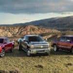 Three Chevrolet trucks from the 2015 lineup parked in grass in front of tall mountains and deep valleys