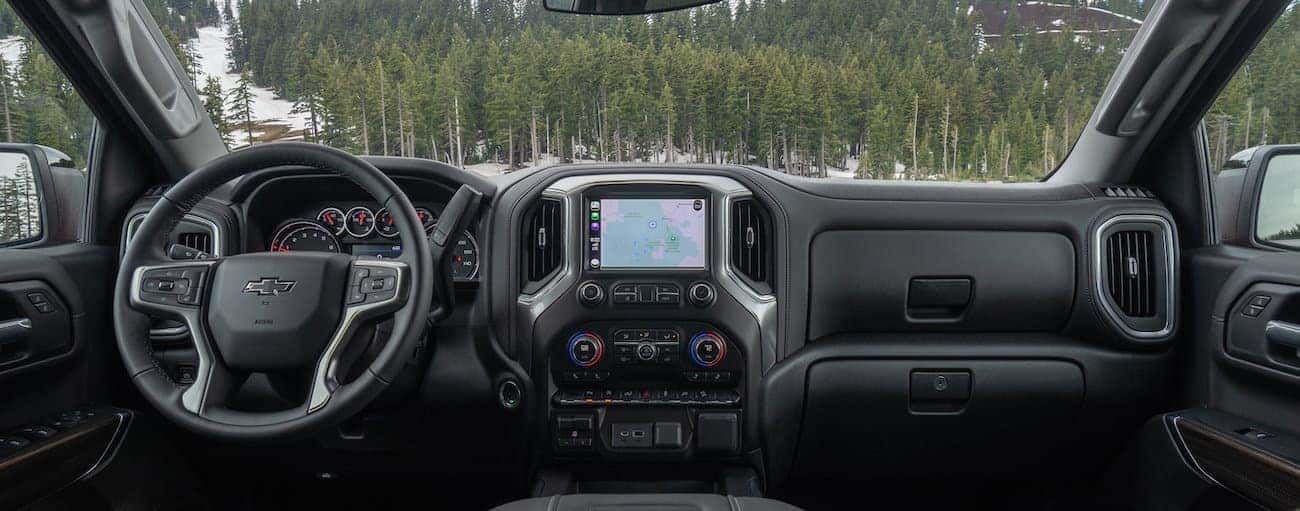 The dashboard and infotainment screen in a 2021 Chevy 1500 are shown with pine trees in the windshield.