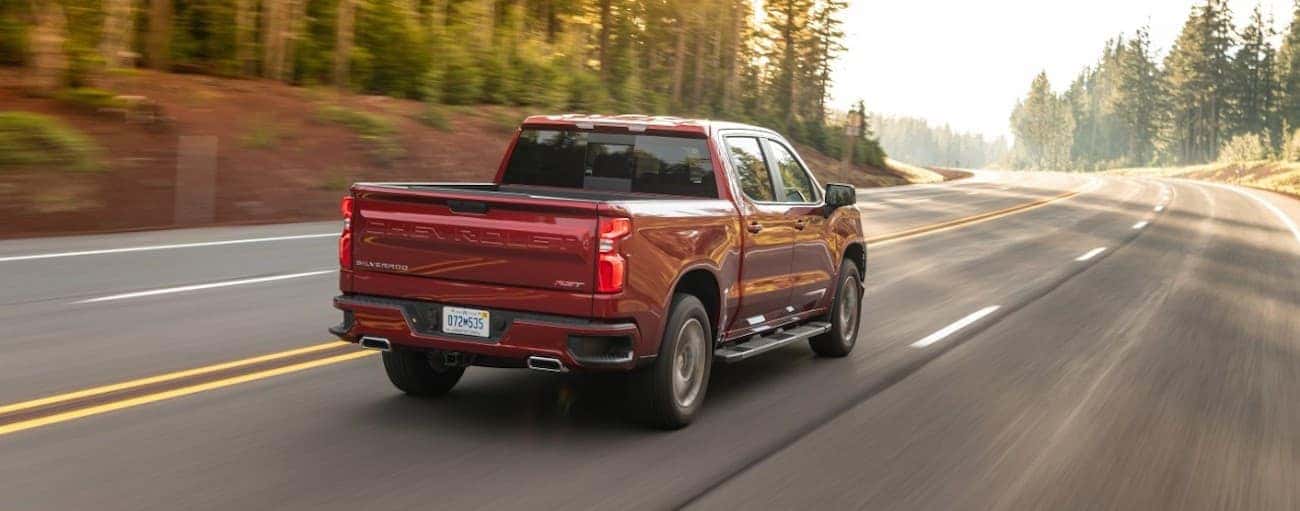 A red 2021 Chevy 1500 diesel is driving on a multi-lane road past pine trees after winning the 2021 Chevy 1500 diesel vs 2021 Ram 1500 diesel comparison.