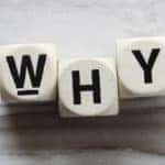 Three white letter die that spell out "WHY" on a grey table